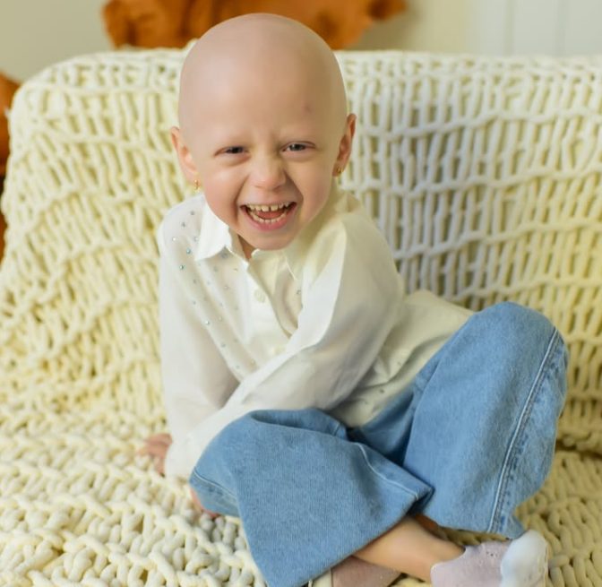 Olivia smiling, sitting on a cream knitted blanket in a white shirt and jeans